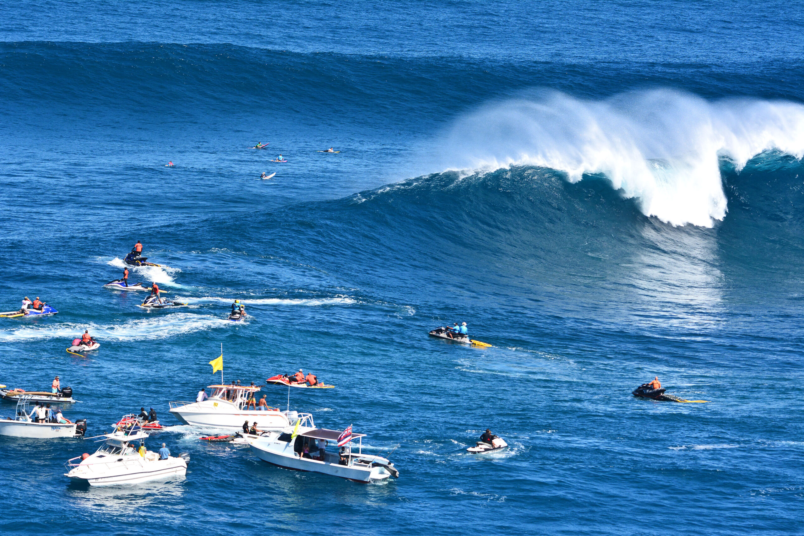 Surfers riding massive waves at Jaws Hawaii, with lush green cliffs in the background