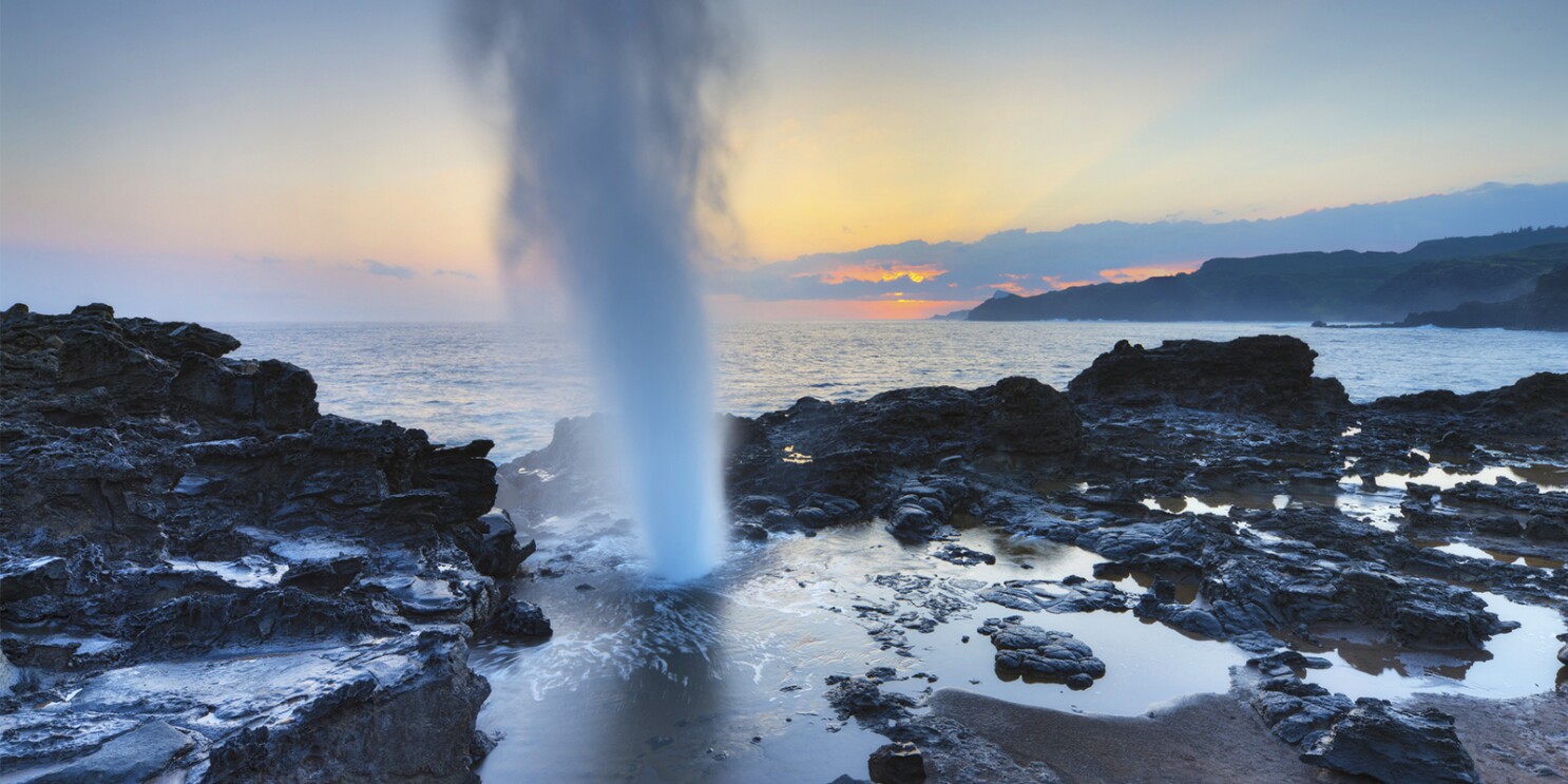 View of a blowhole in Hawaii, showcasing the spectacular spray of water shooting high into the air against a backdrop of the ocean.